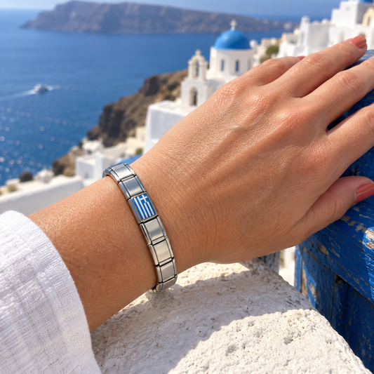 Greek flag Italian charm on a polished silver starter bracelet worn on a Santorini terrace overlooking the Aegean Sea