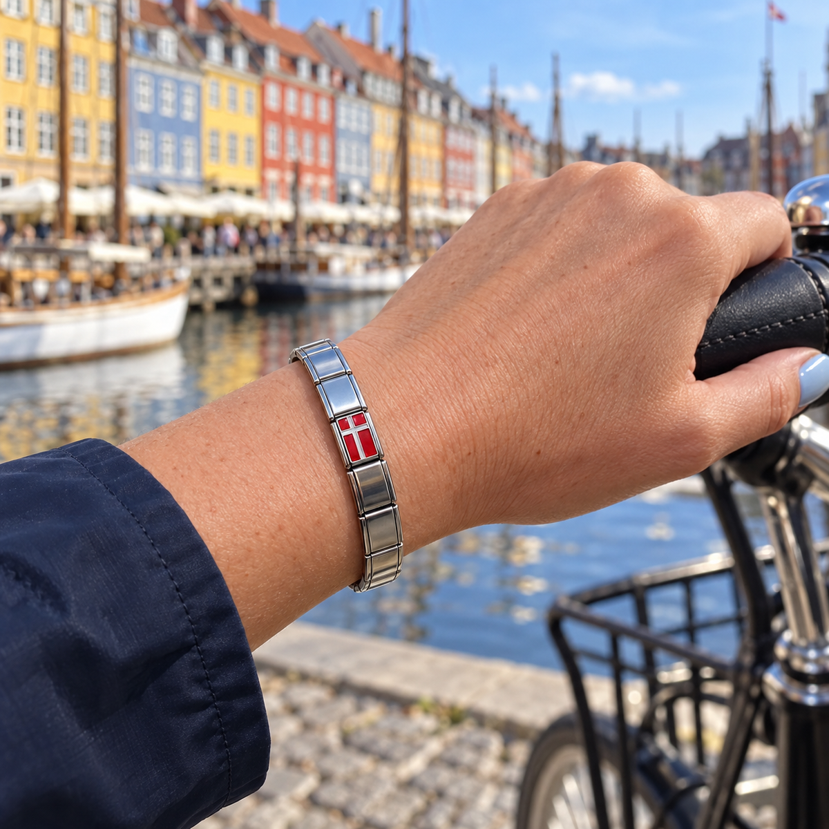 Denmark flag Italian charm on a polished silver bracelet beside a bicycle at Copenhagen’s Nyhavn waterfront
