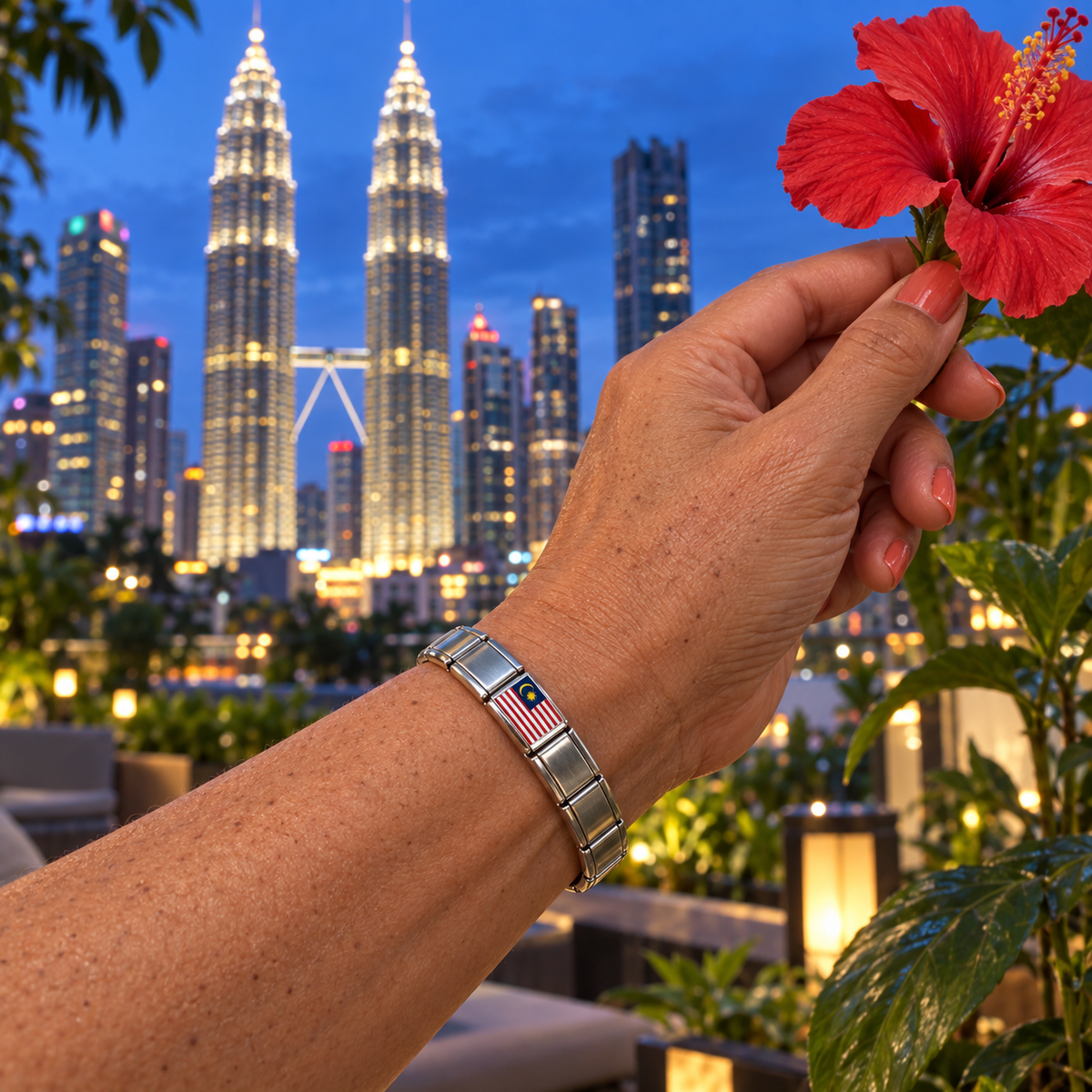 Malaysia flag Italian charm on a silver charm bracelet worn against the illuminated Petronas Twin Towers with a red hibiscus
