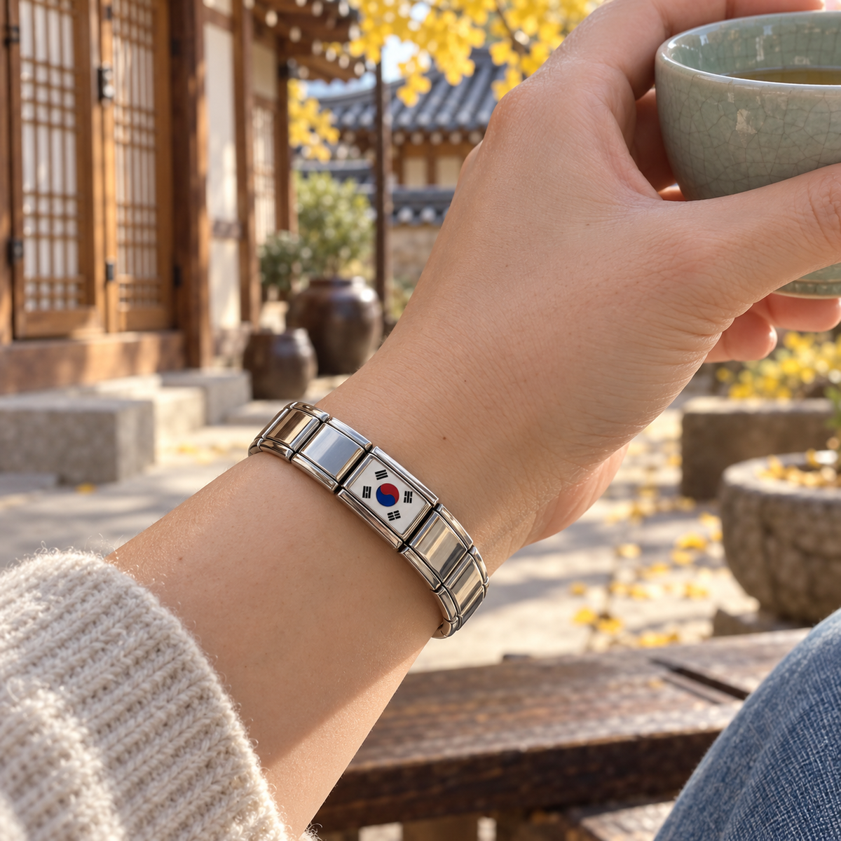 South Korea flag Italian charm on a shiny silver bracelet worn while holding a celadon tea cup in a traditional Korean hanok courtyard
